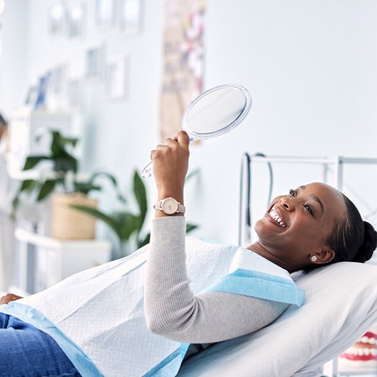 Woman smiling at reflection in handheld mirror
