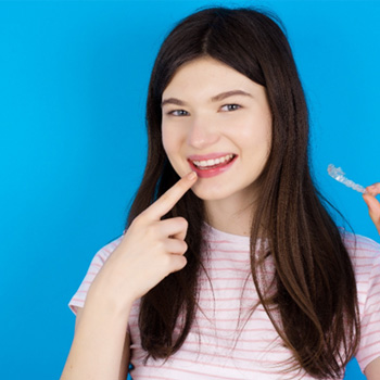 Female holding Invisalign aligner and pointing to her smile 