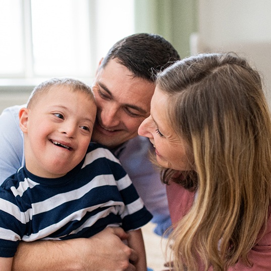 Man and woman hugging boy in striped shirt