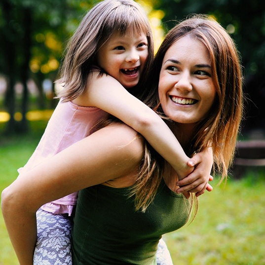 Woman in green shirt giving piggy-back ride to little girl outside