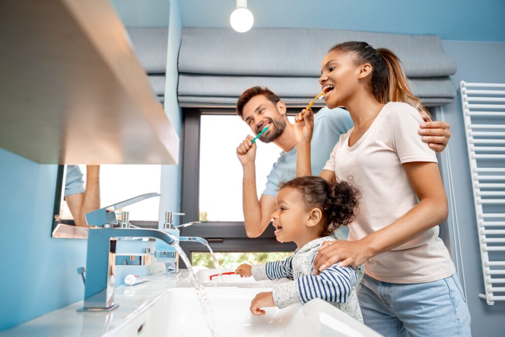 Woman, man, and girl brushing teeth together in blue bathroom