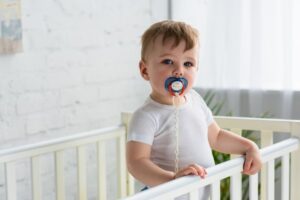 Baby standing in crab with pacifier in his mouth. 