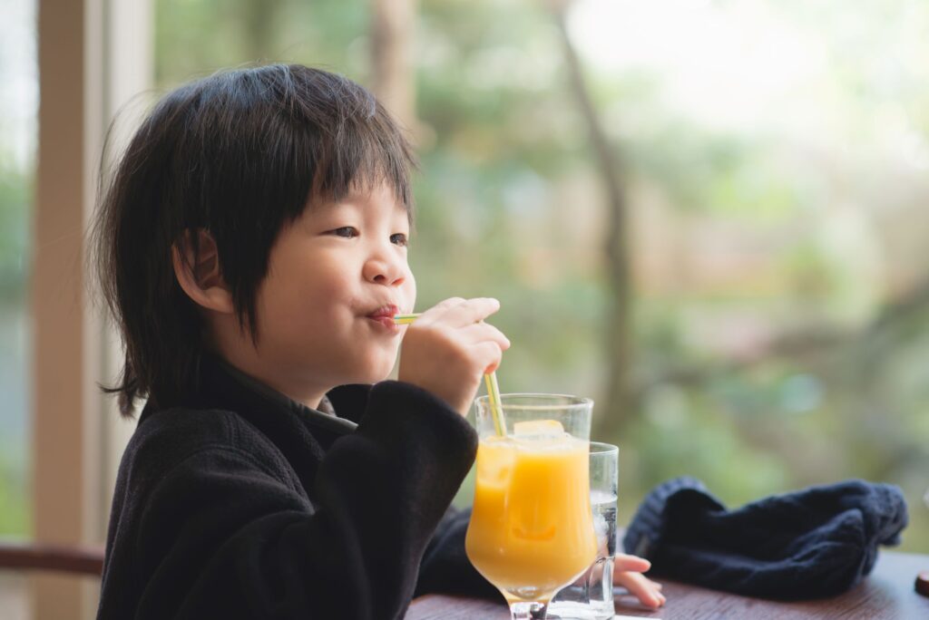 Kid wearing black shirt drinking juice out of a fancy glass with straw